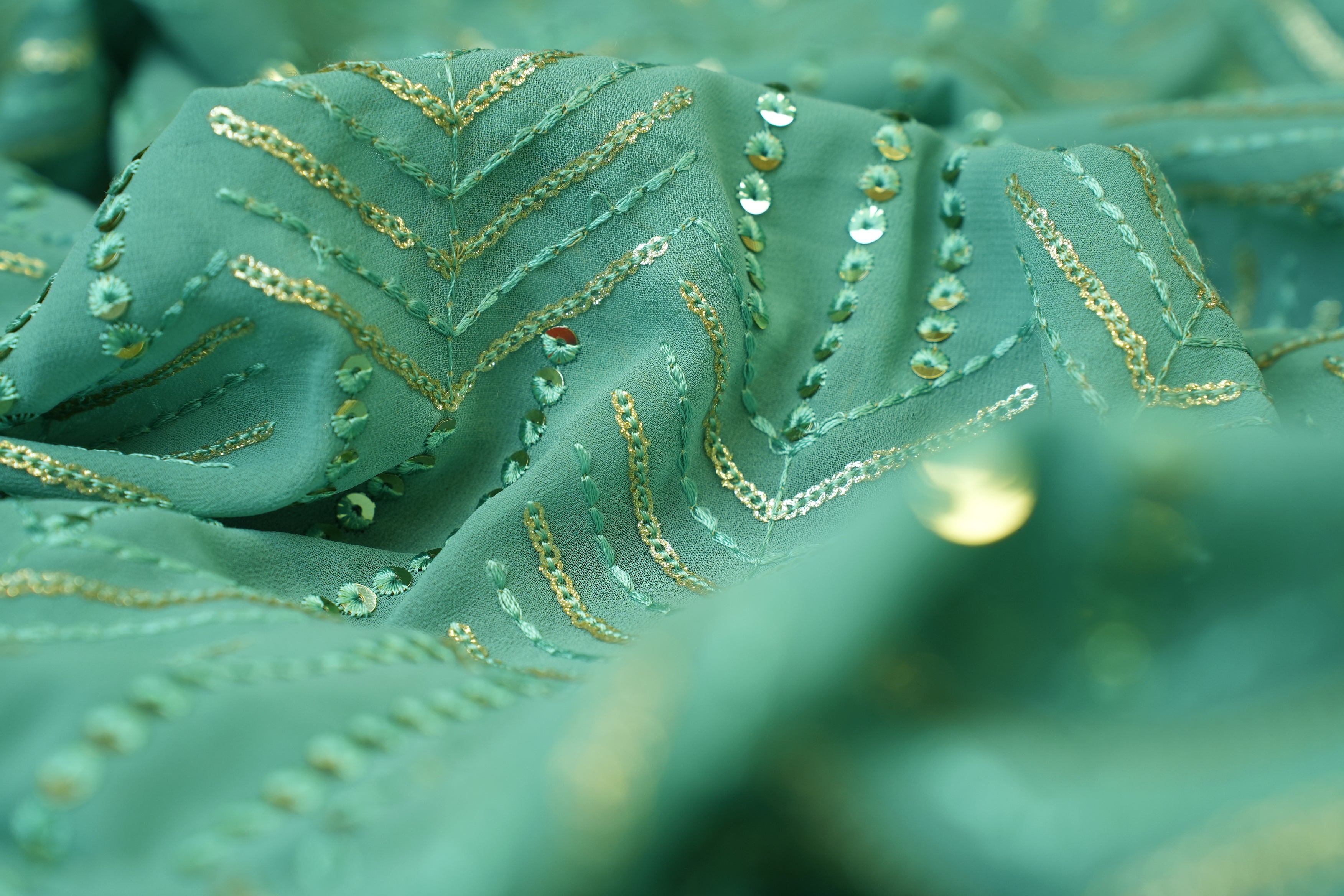 Thread work with golden sequins creating abstract pattern on teal georgette fabric