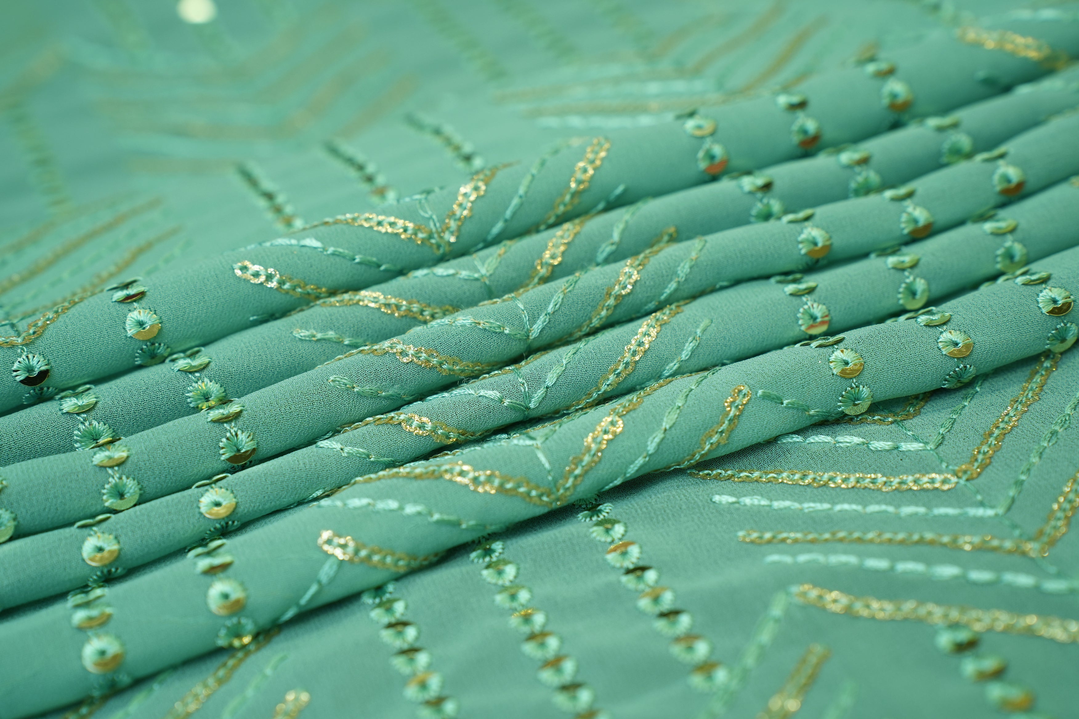 Thread work with golden sequins creating abstract pattern on teal georgette fabric